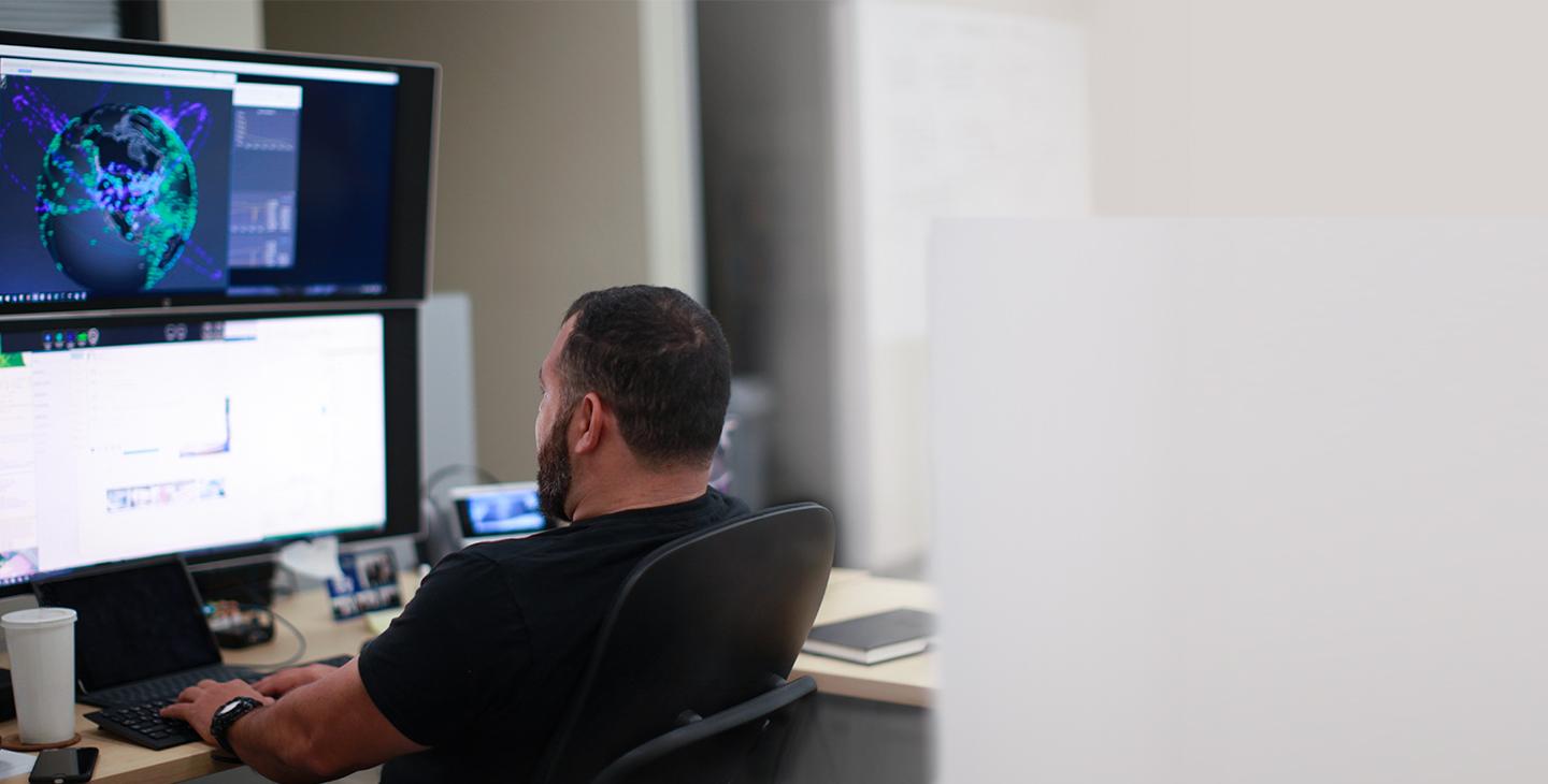 Man sitting at a desk looking at two monitors stacked on top of each other and typing on a keyboard